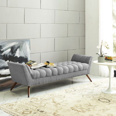 A grey upholstered bench in front of a painting.